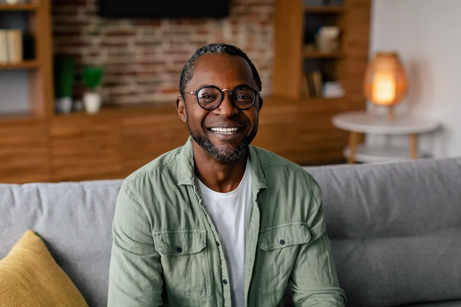 Andropause-Doctor A middle aged black man in a green button up shirt sits on his couch smiling, happy with his treatment for andropause and low testosterone from AZENA Health & Longevity in Gainesville.