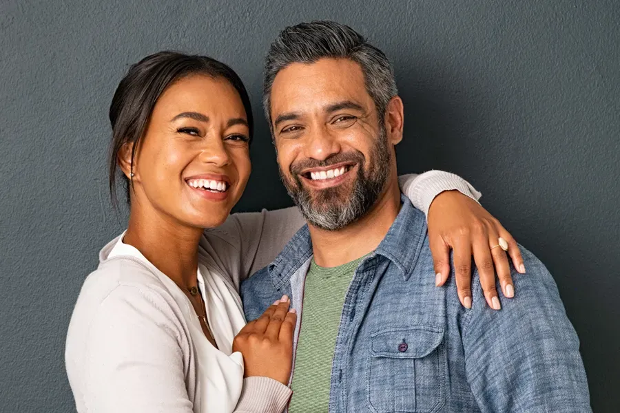Bioidentical-Hormone-Therapy-Doctor A middle-aged couple with their arms around each other standing against a gray background and smiling, happy with the bioidentical hormone therapy they received from AZENA Health & Longevity in Gainesville.