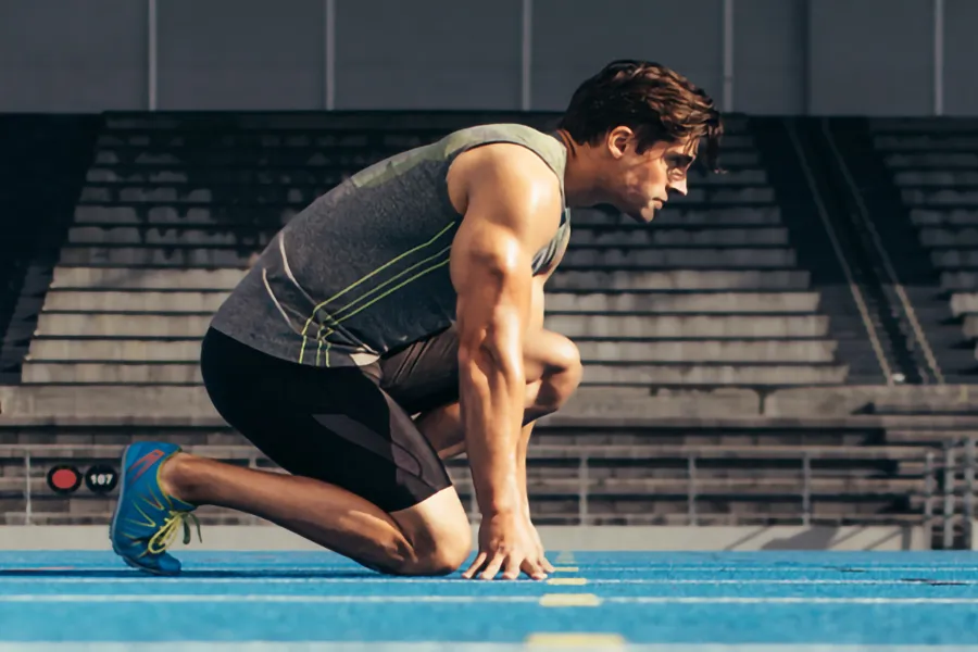 Lean-Muscle-and-Recovery-Clinic A white man kneels at the starting line on a track, determined to do his best. Get treatment for lean muscle loss and recovery from AZENA Health & Longevity in Gainesville.