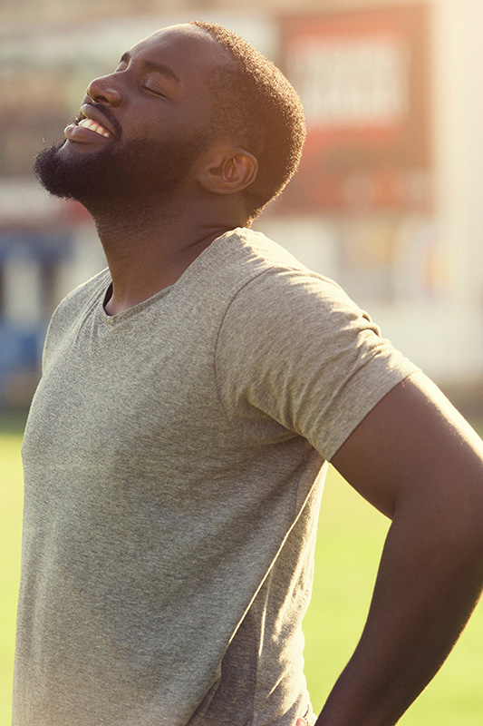Lean-Muscle-and-Recovery-Treatment A black man in a gray t-shirt and smiles, looking up with closed eyes after a satisfying workout. Get treatment for lean muscle loss and recovery from AZENA Health & Longevity in Gainesville.