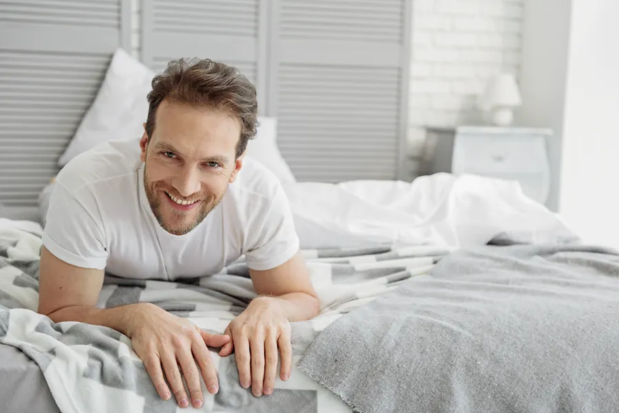Low-Libido-in-Men-Doctor A dirty-blonde haired man lays on his stomach in bed smiling. Schedule treatment for low libido in men from AZENA Health & Longevity in Gainesville.