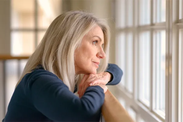 PMDD-Specialist A middle-aged woman with with a somber expression stares out the window. Get treatment for Premenstrual Dysphoric Disorder from AZENA Health & Longevity in Gainesville.