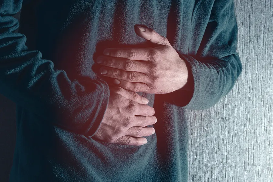 Ulcerative-Colitis-Clinic Close-up of the midsection of a man in a green sweater clutching his gut in pain. Get treatment for Ulcerative Colitis from AZENA Health & Longevity in Gainesville.